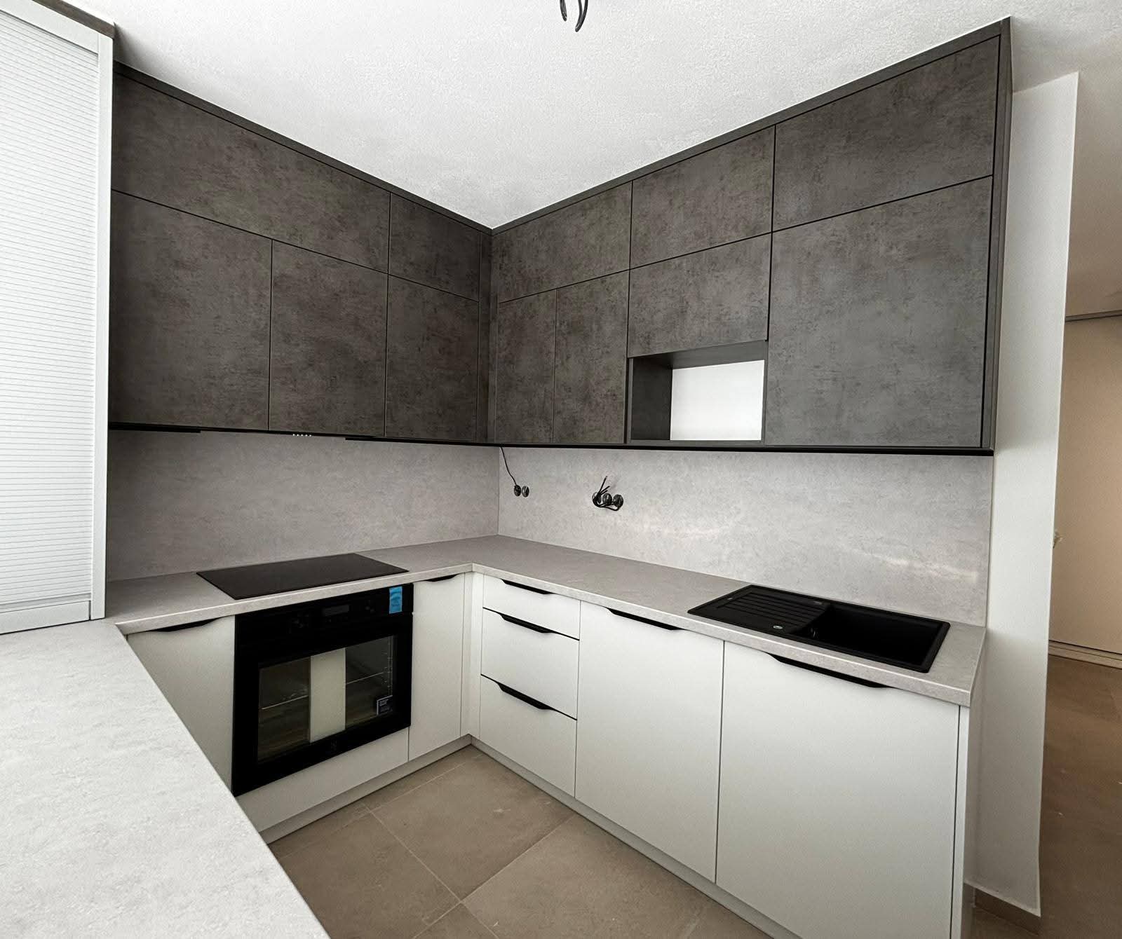 Paneláková kuchyně, která ukazuje, že i menší prostor může působit moderně a stylově. Kombinace dekoru Beton Chicago v tmavě šedé s jemnou smetanově bílou vytváří nadčasový kontrast, který jen tak neomrzí.  Celkový vzhled podtrhují elegantní tulip úchytky, které dodávají kuchyni čistý a uhlazený výraz. Praktické řešení do každodenního provozu, kde má všechno své místo – a zároveň radost na pohled.