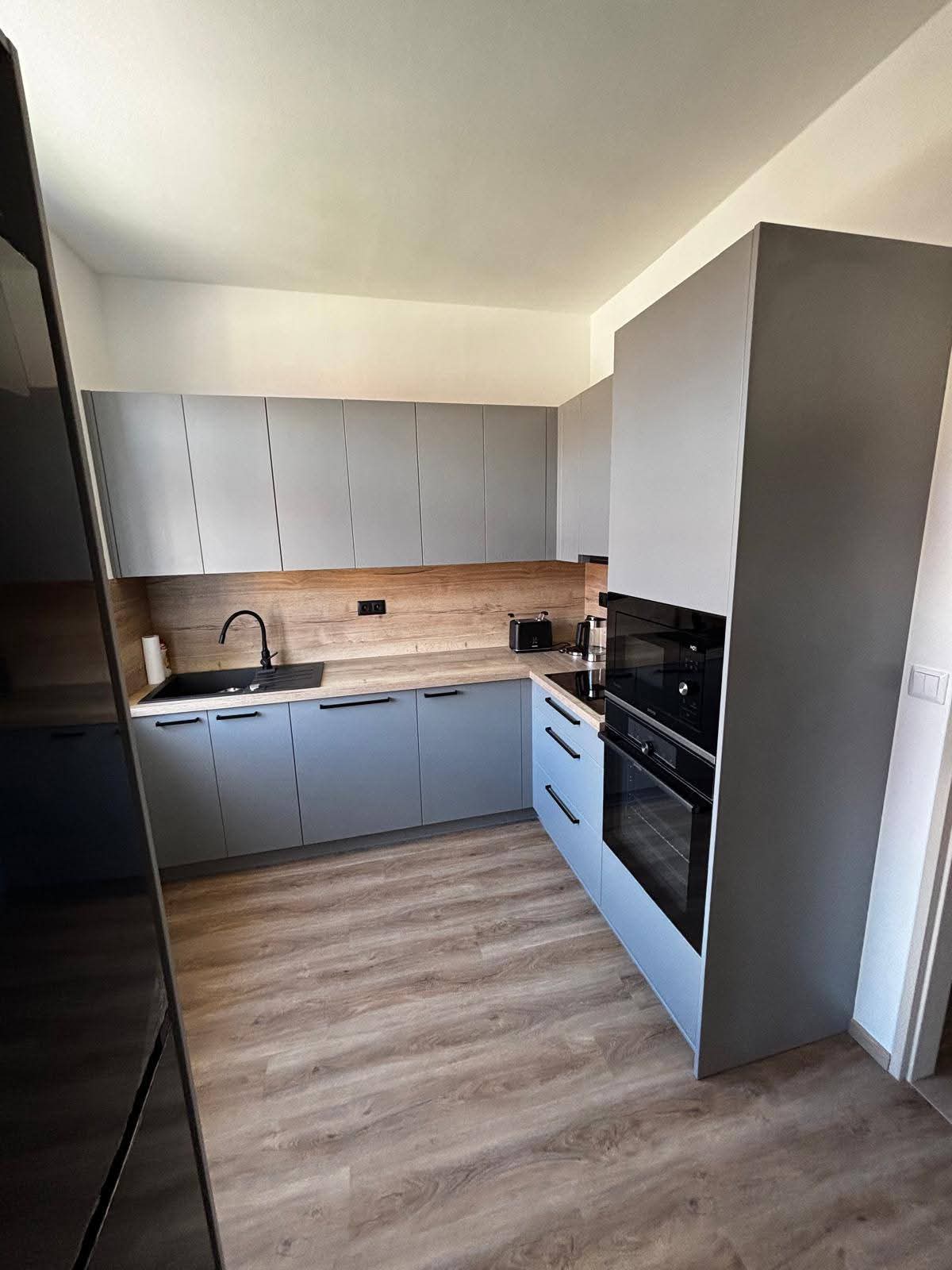 Kuchyně v panelovém bytě v elegantním dekoru prachově šedé působí čistě, moderně a nadčasově. Kombinace světlého, neutrálního tónu s výraznou zástěnou v dekoru Dub Halifax přírodní dodává prostoru příjemné teplo a kontrast.  Dekor Dub Halifax je typický svou autentickou kresbou dřeva s výraznými suky a prasklinami, které působí velmi přirozeně a živě . Díky tomu kuchyně nepůsobí sterilně, ale naopak útulně i v menším panelákovém prostoru.  Celkový dojem podtrhuje jednoduchý design bez zbytečností – funkční řešení, které maximálně využívá prostor a zároveň si zachovává estetickou lehkost.